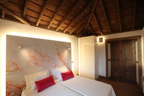 A bedroom with a wooden ceiling, a bed with white bedding and red pillows, a white wall with orange paint splatter, and a wooden door. - Luxury villa with heated pool and exceptional sea and canyon views, (Barlovento)