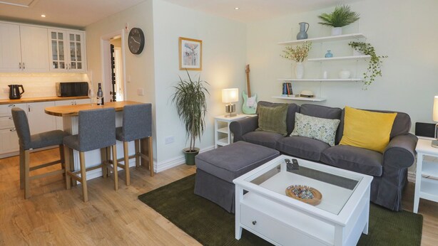 A modern living room with a dining area, a sofa set, a coffee table, and a kitchen in the background. - Drapers Cottage (Grange-over-Sands)
