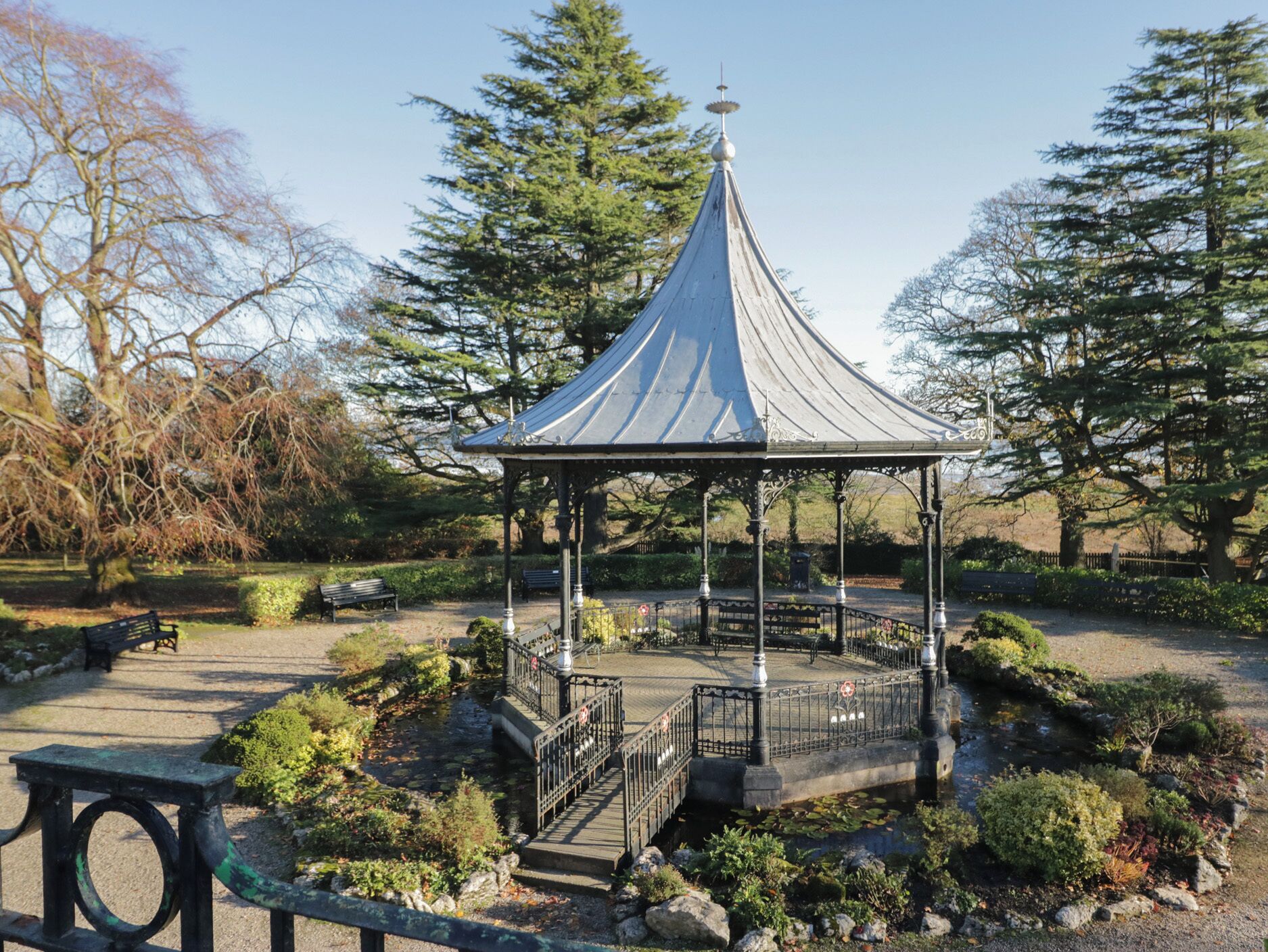 Un kiosque surmonté d’un toit conique, entouré d’un jardin où poussent différentes espèces de plantes et agrémenté d’un petit étang.