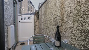 A narrow alleyway with a green metal table and two wine glasses, a bottle of wine, and a white door. - Drapers Cottage (Grange-over-Sands)