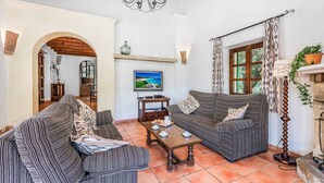A cozy living room with striped sofas, a wooden coffee table, and a television on the wall. - Finca Cas Tomas | Cala San Vicente | Traditional charm and mountain views |. (Pollensa)