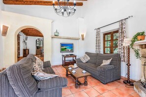 A cozy living room with striped sofas, a wooden coffee table, and a television on the wall. - Finca Cas Tomas | Cala San Vicente | Traditional charm and mountain views |. (Pollensa)