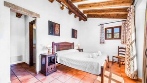A bedroom with a wooden ceiling, a bed, a nightstand, a chair, and a window with curtains. - Finca Cas Tomas | Cala San Vicente | Traditional charm and mountain views |. (Pollensa)