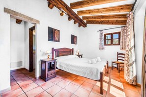 A bedroom with a wooden ceiling, a bed, a nightstand, a chair, and a window with curtains. - Finca Cas Tomas | Cala San Vicente | Traditional charm and mountain views |. (Pollensa)
