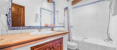 A bathroom with a wooden vanity, a white sink, a mirror with a blue frame, a toilet, and a bathtub.