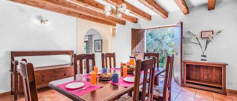 Un comedor con muebles de madera, una mesa dispuesta con platos, tazas y una cesta de fruta.