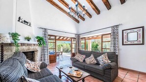 A spacious living area with a fireplace, two sofas, a coffee table, and large windows offering a view of the outdoors. - Finca Cas Tomas | Cala San Vicente | Traditional charm and mountain views |. (Pollensa)
