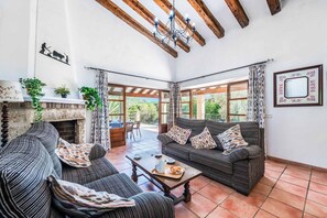 A spacious living area with a fireplace, two sofas, a coffee table, and large windows offering a view of the outdoors. - Finca Cas Tomas | Cala San Vicente | Traditional charm and mountain views |. (Pollensa)