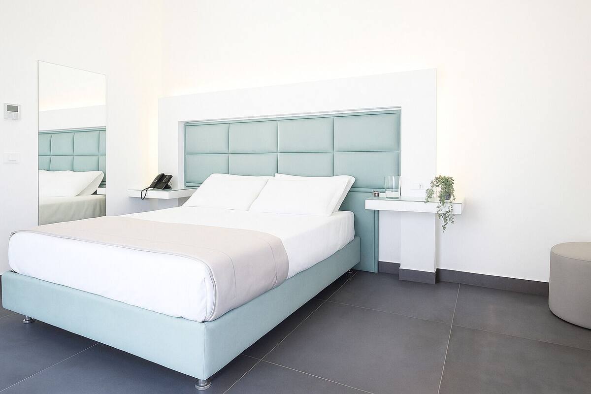 A modern hotel room with a bed, bedside tables, a mirror, and a small plant.