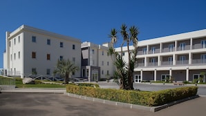 Un hotel moderno de varios pisos con fachada plana, balcones y un patio ajardinado con palmeras.