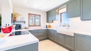 Een moderne keuken met grijze kastjes, een wit aanrecht en een raam met uitzicht op groen.