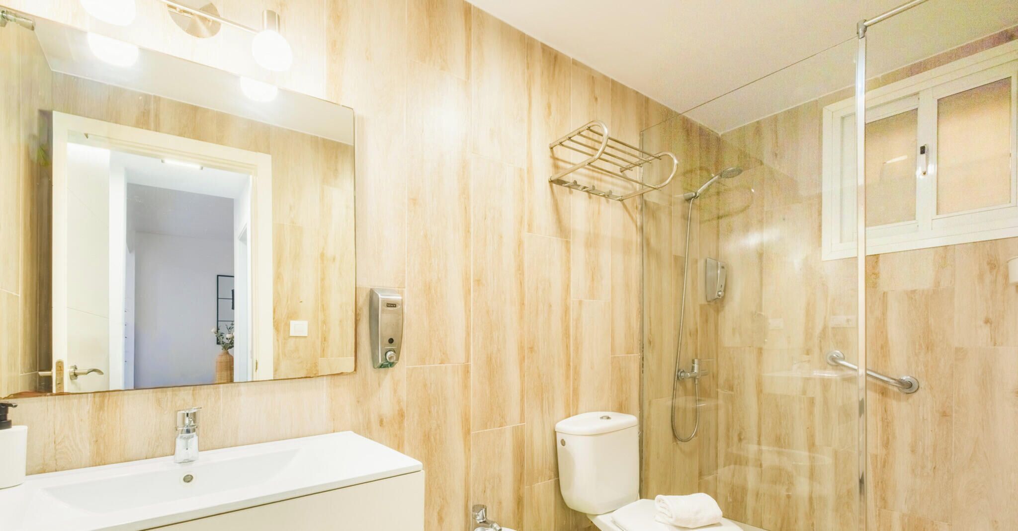 A bathroom with a wooden wall, a sink, a toilet, a shower, and a mirror.