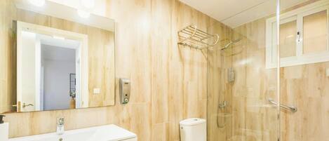 A bathroom with a wooden wall, a sink, a toilet, a shower, and a mirror.