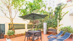 Un patio al aire libre con una mesa y sillas, un parasol y sillones de descanso.