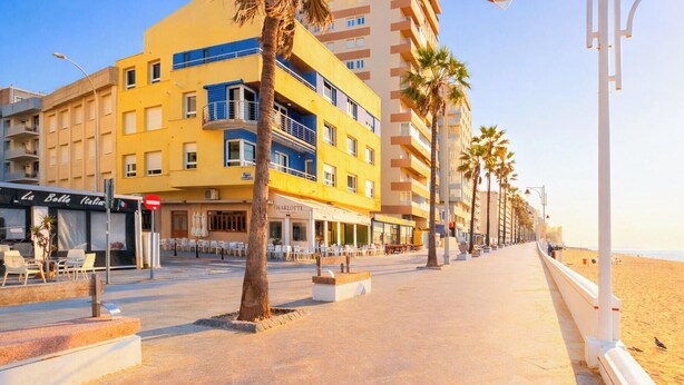 Un paseo marítimo con una hilera de edificios, incluyendo un edificio amarillo con balcones y un restaurante llamado 'Charlotte'.