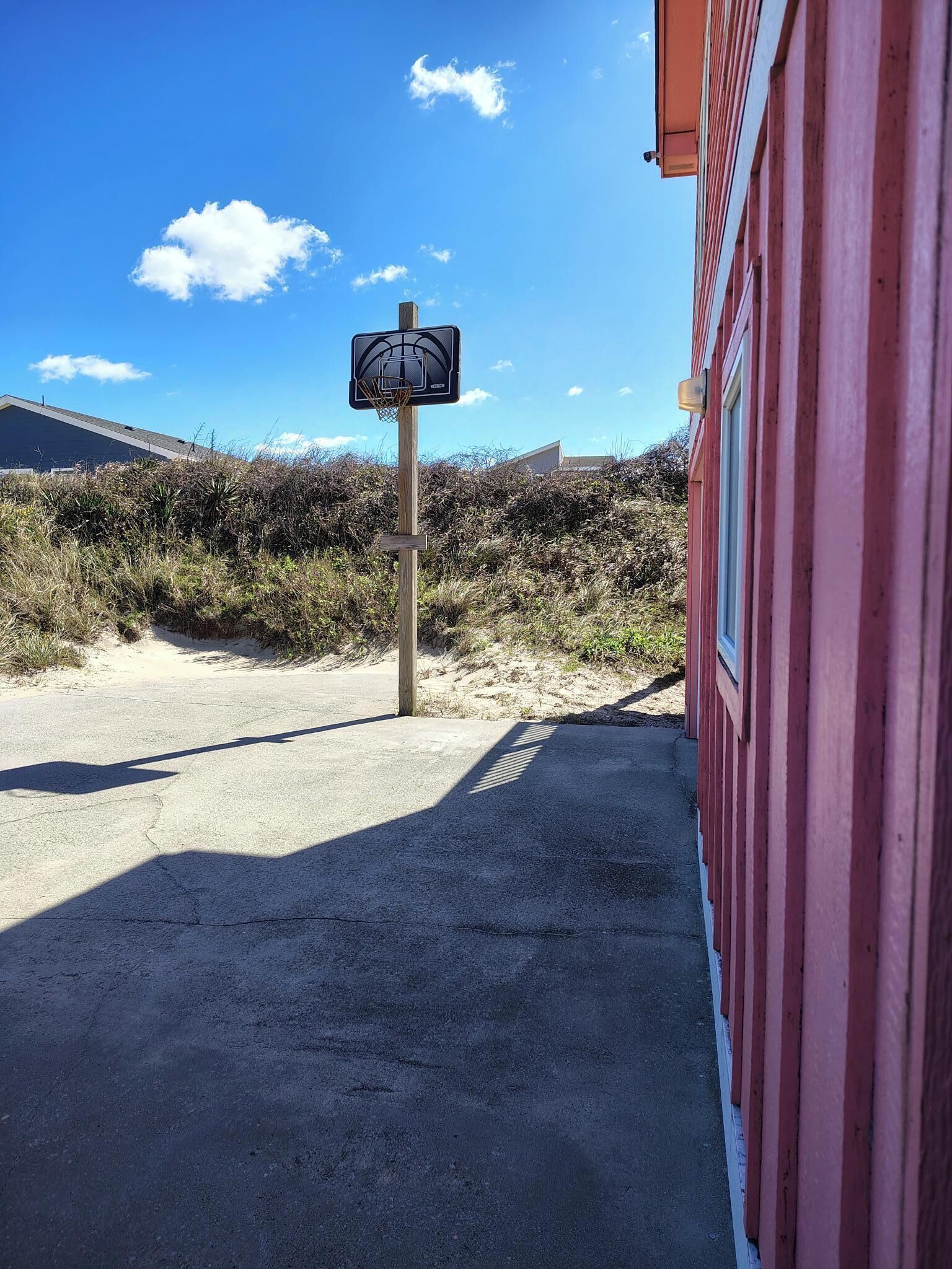 A basketball hoop in a sandy area with a red building in the background.