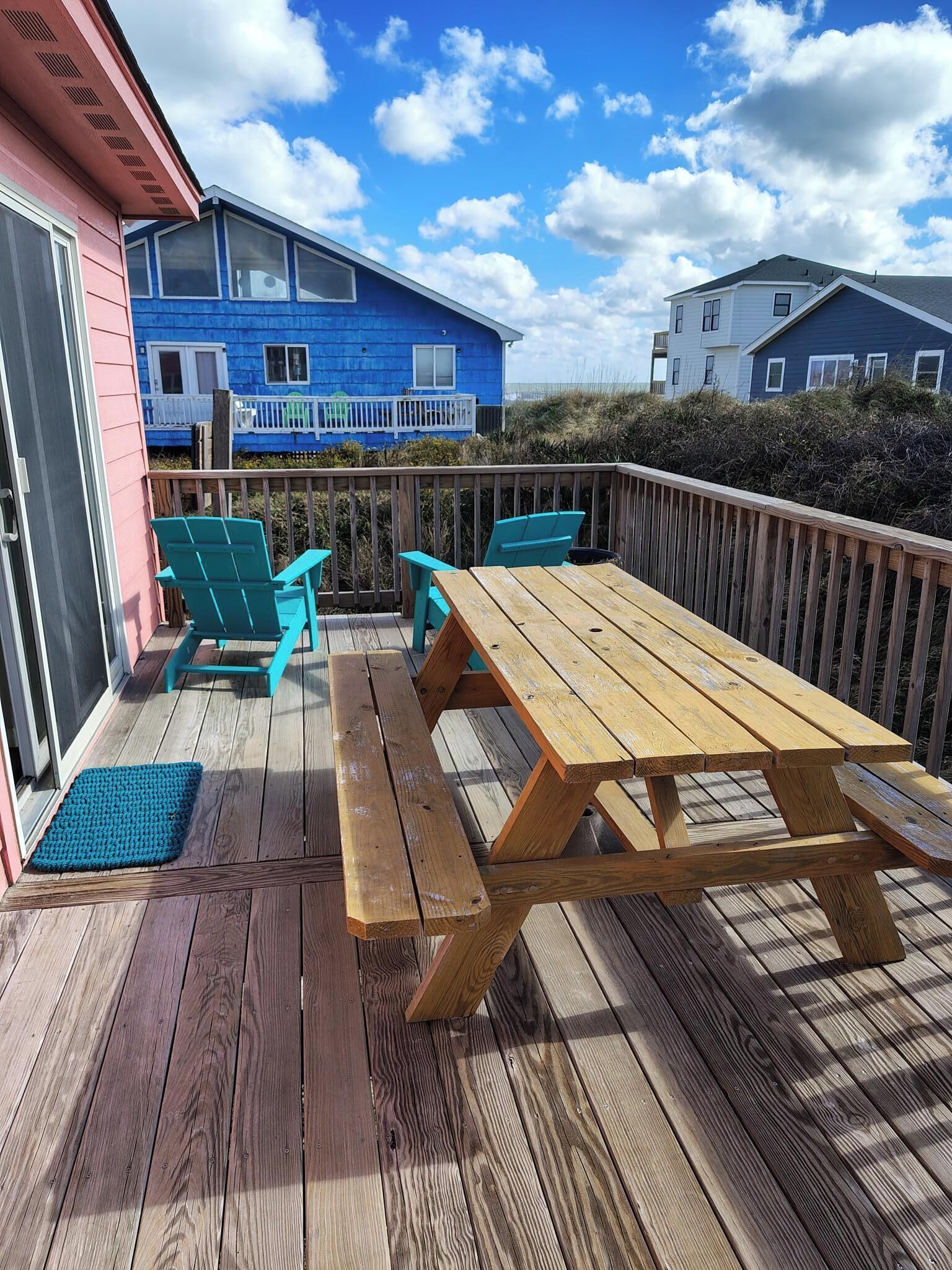 A wooden deck with a picnic table and chairs, a blue house in the background, and a clear sky.