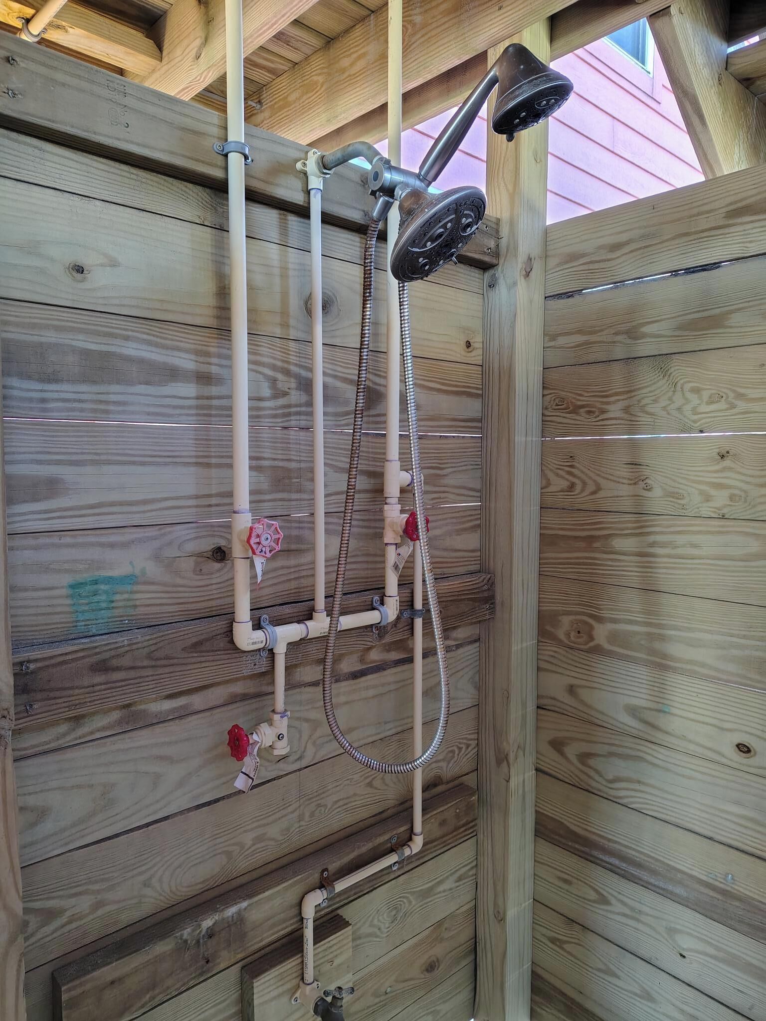 A wooden shower enclosure with a handheld showerhead and a handheld shower attachment.