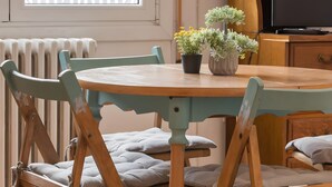 Un comedor con una mesa redonda, sillas de madera, una planta en maceta y un televisor.