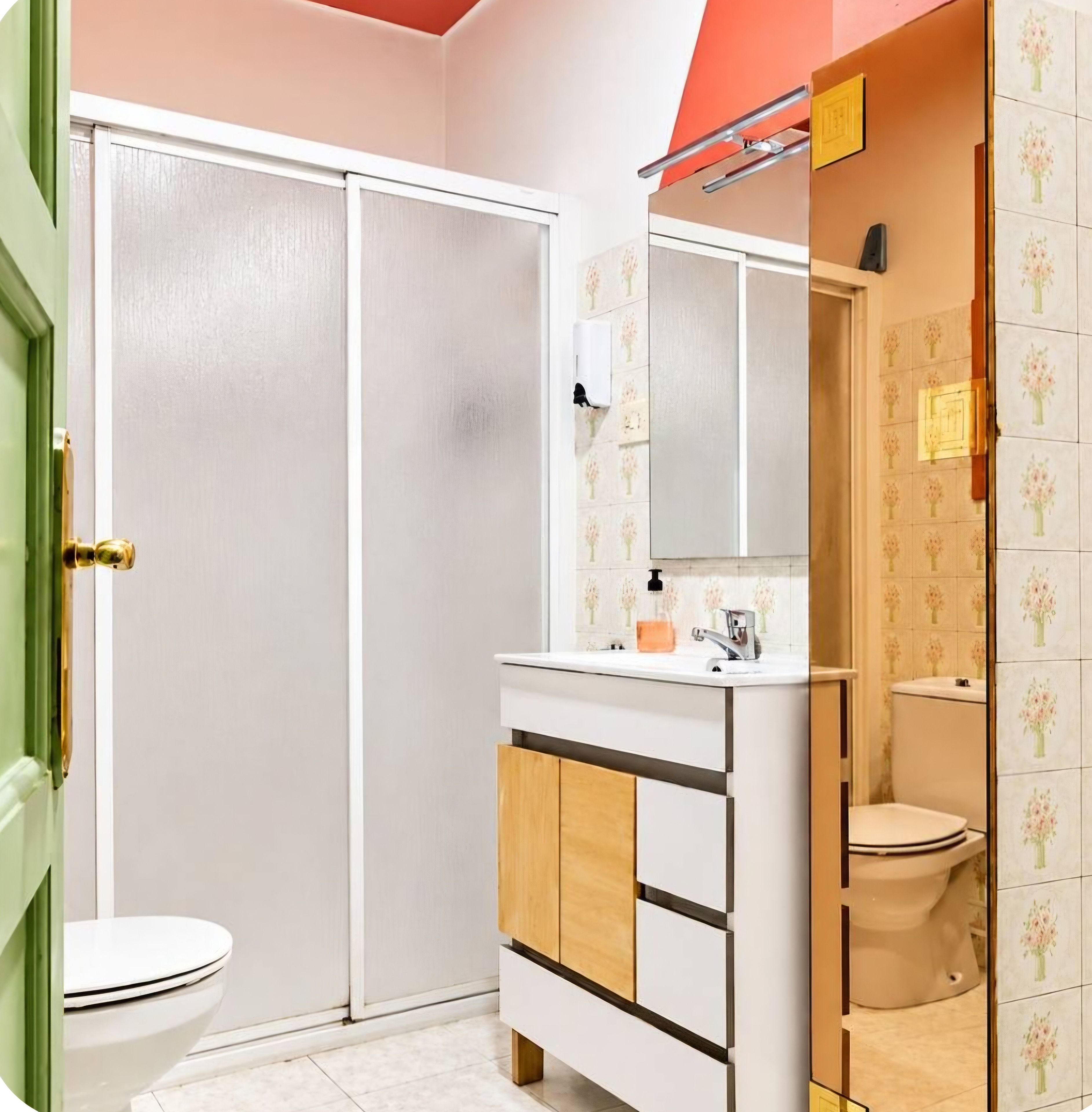 Un baño con inodoro, lavamanos con espejo y zona de ducha.