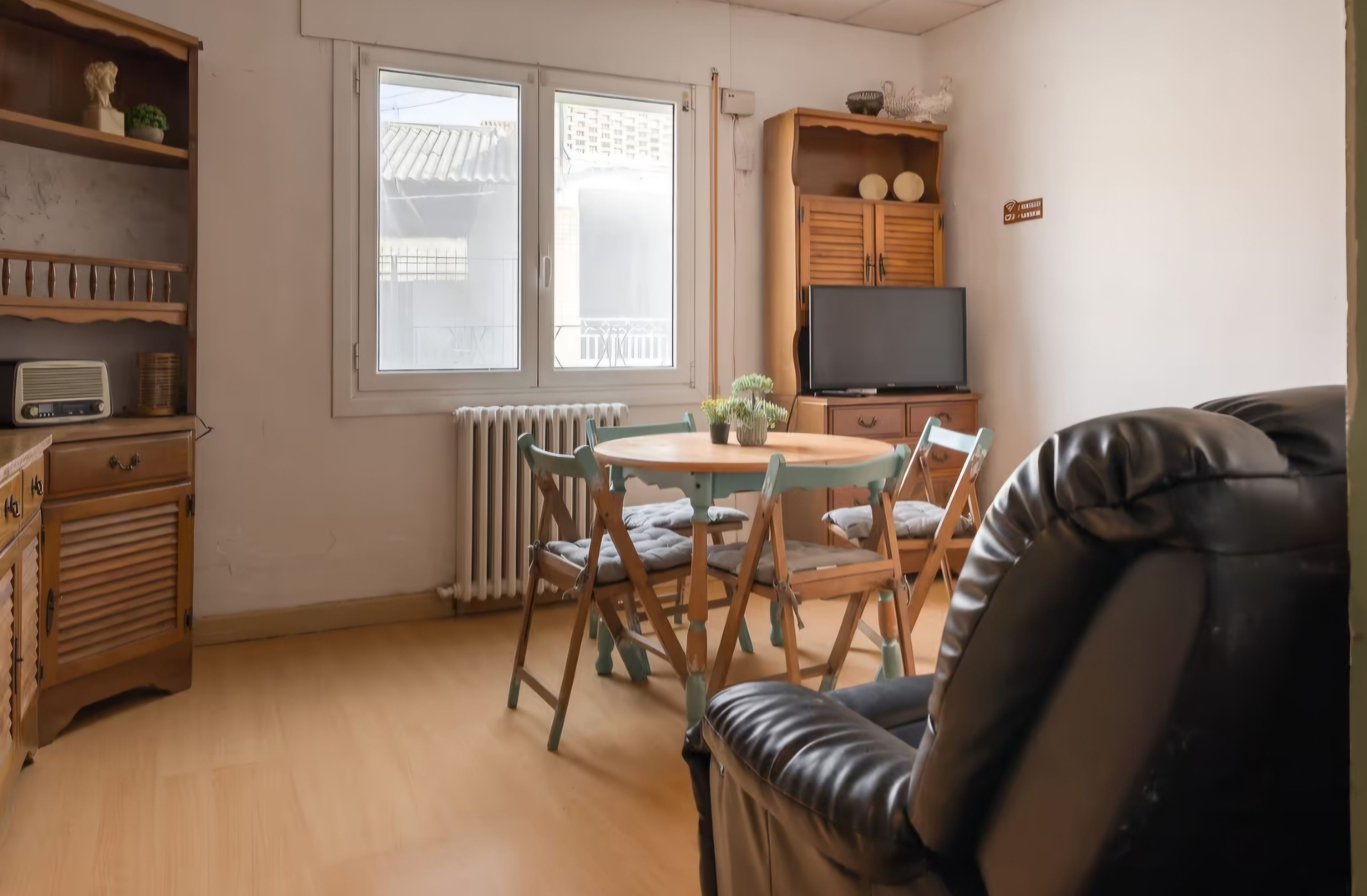 Una sala de estar acogedora con una mesa de comedor de madera, sillas, un sofá de cuero, un televisor y un radiador.