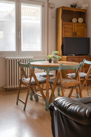 Ein Zimmer mit einem Holzespeise Tisch, Stühlen, einer schwarzen Ledercouch, einem Fernseher und einer Holzkabine mit Dekorationsgegenständen.