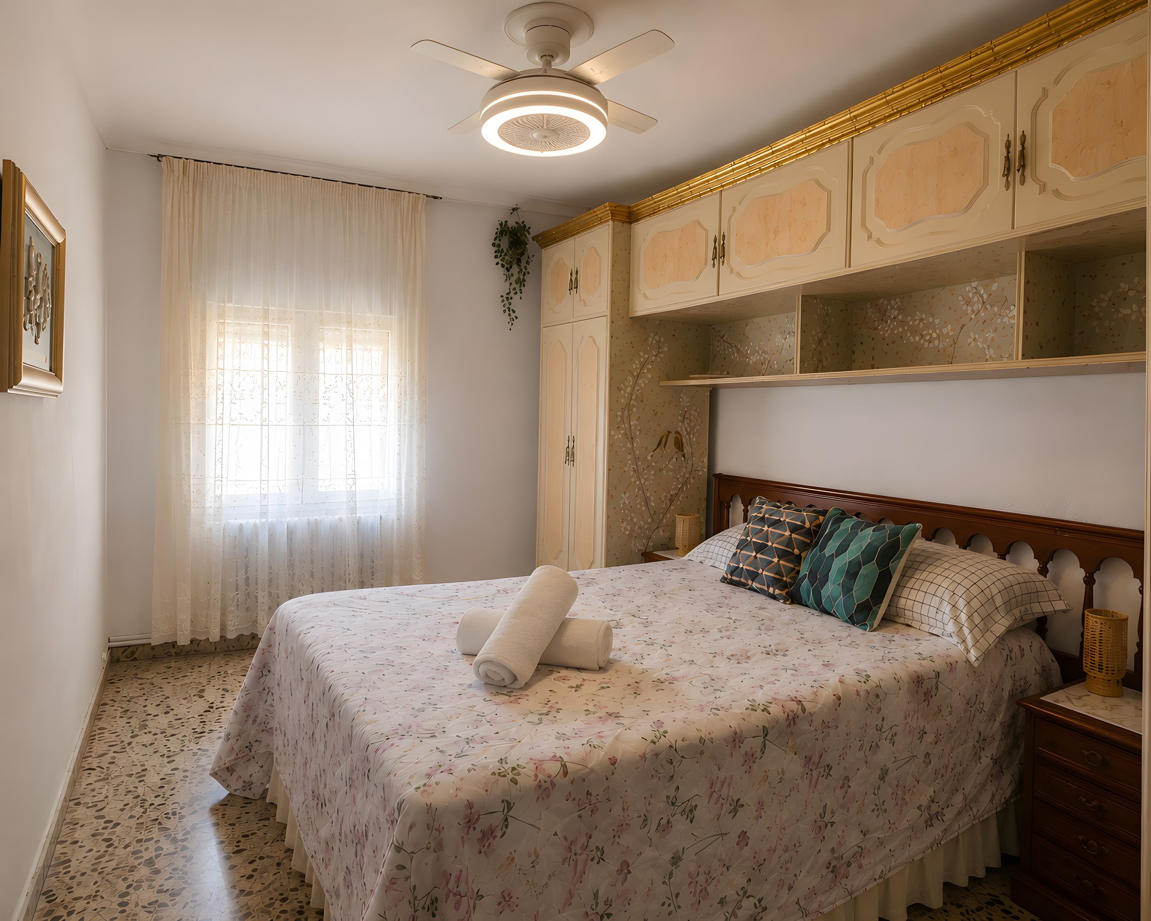 Un dormitorio con cama, ventilador de techo, ventana con cortinas y armario.
