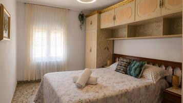 Un dormitorio con cama, ventilador de techo, ventana con cortinas y armario.