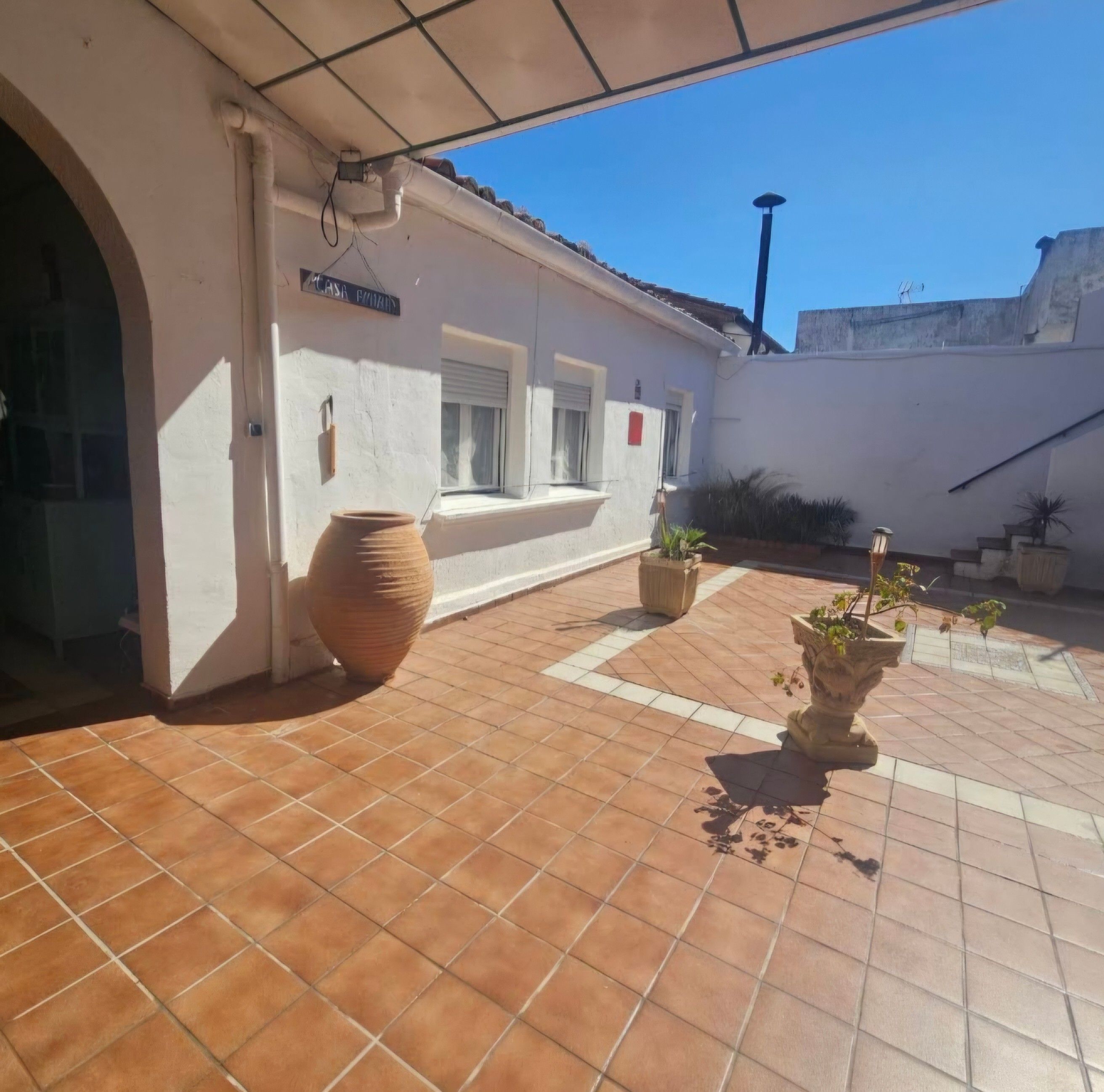 Un patio con piso de baldosas, una maceta de barro grande y plantas en macetas.