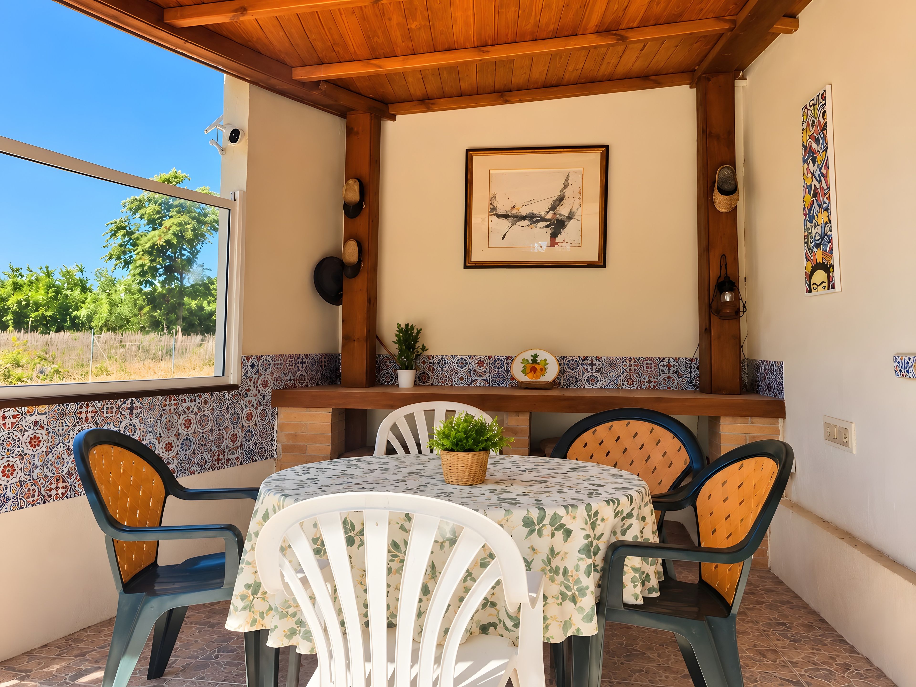A patio with a table and chairs, a wooden ceiling, a tiled backsplash, and a framed picture on the wall.