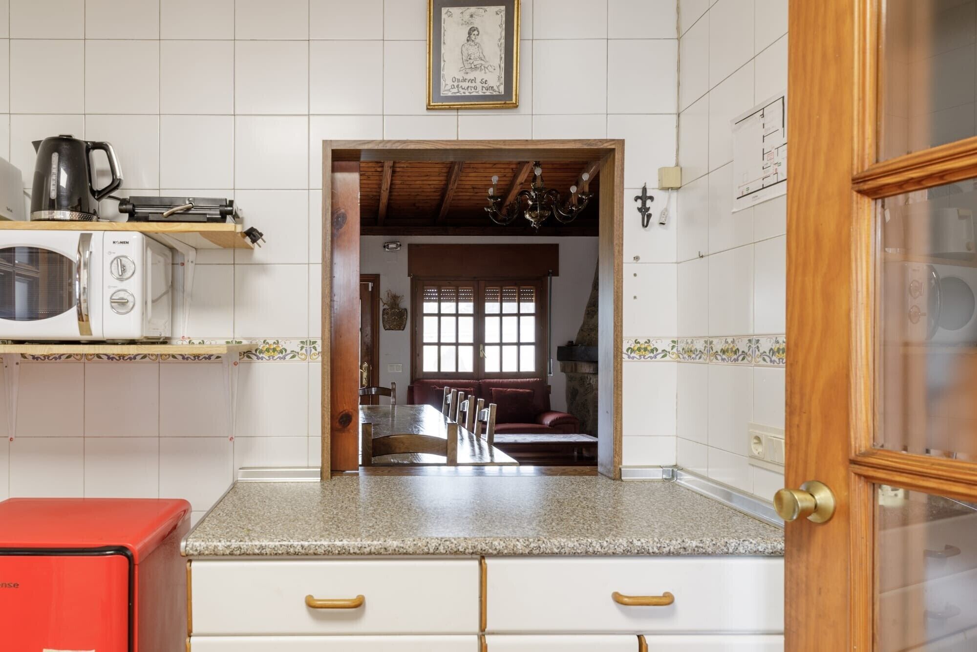 Una cocina con un microondas, un electrodoméstico rojo y una puerta de madera.