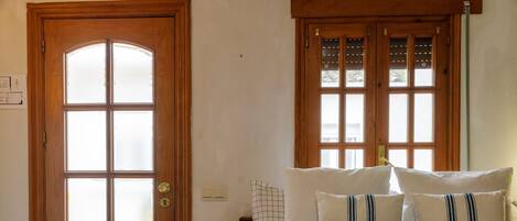 Una habitación con puerta de madera, una cama con muchos almohadones y una ventana con persianas.