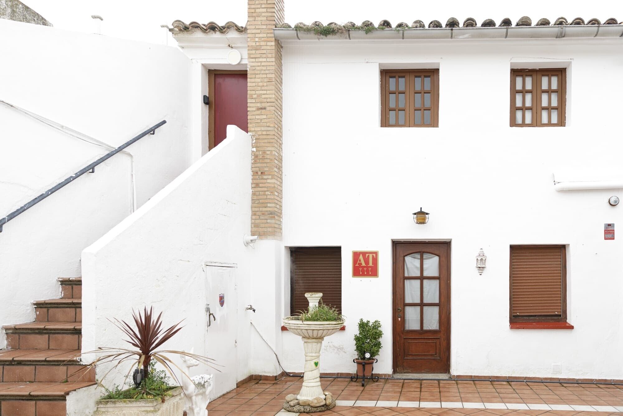 Un edificio blanco con una puerta roja, una ventana y un cartel que dice 'AT'.