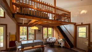 Une pièce de style loft avec un escalier en bois, une table à manger, une chaise et une fenêtre donnant sur une forêt.
