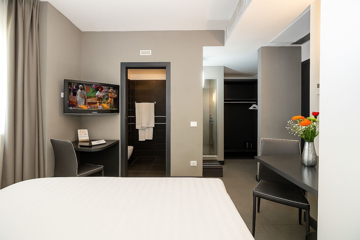 A hotel room with a bed, a desk, a TV, a shower, and a closet.