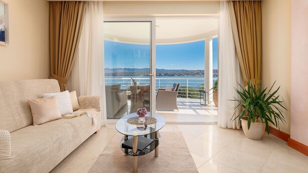 Uma sala de estar com sofá, mesa de centro de vidro e vista para uma varanda com mobiliário de exterior.