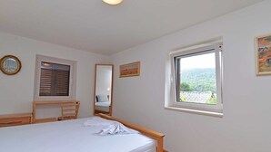 Ein Schlafzimmer mit Bett, Schreibtisch, Stuhl, Fenster mit Aussicht, Spiegel und einem Wandbild.