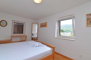 Ett sovrum med en säng, ett skrivbord, en stol, ett fönster med utsikt, en spegel och en tavla som hänger på väggen.