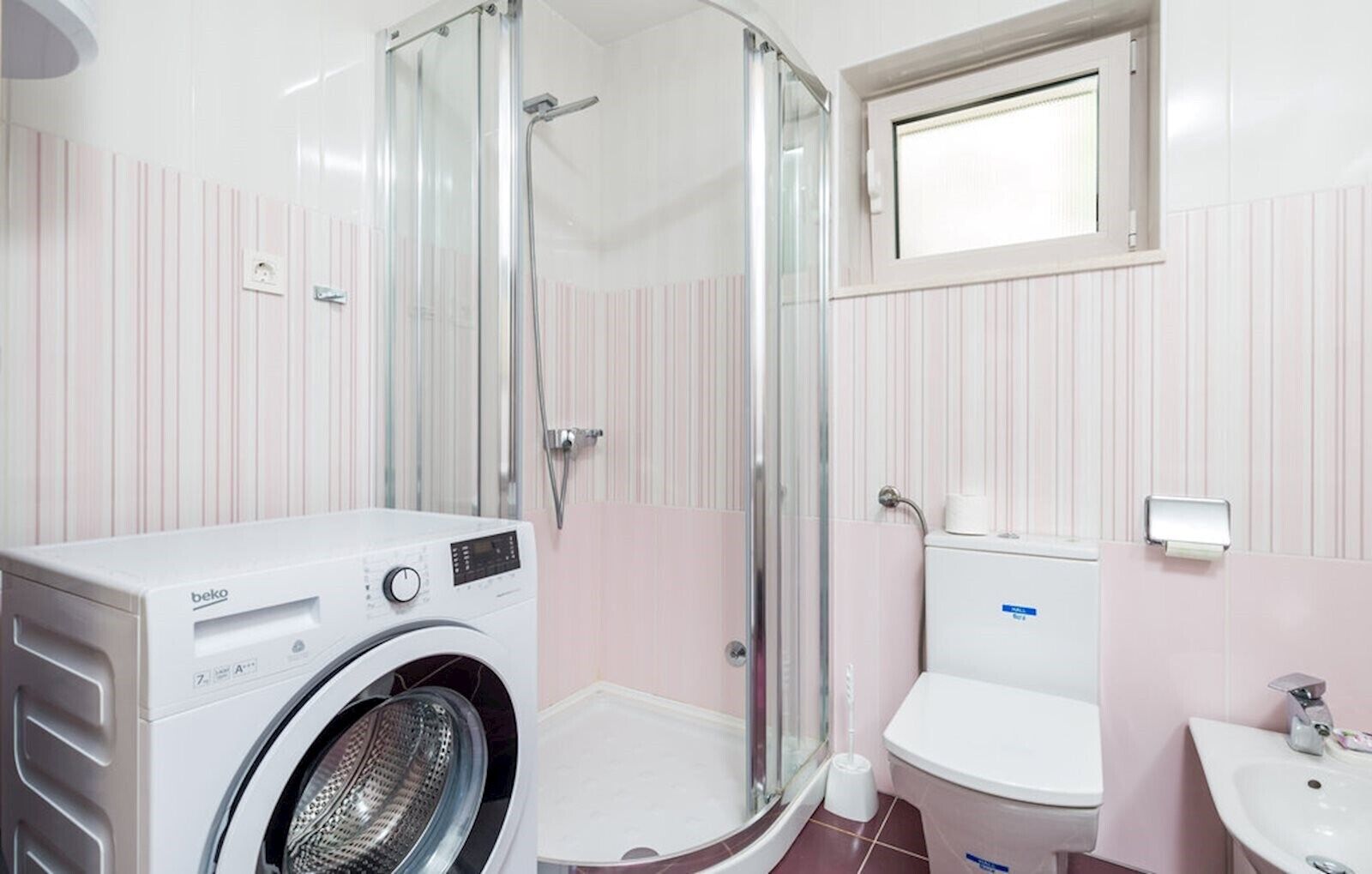 Un baño pequeño con lavadora, cabina de ducha de vidrio, inodoro y lavamanos.