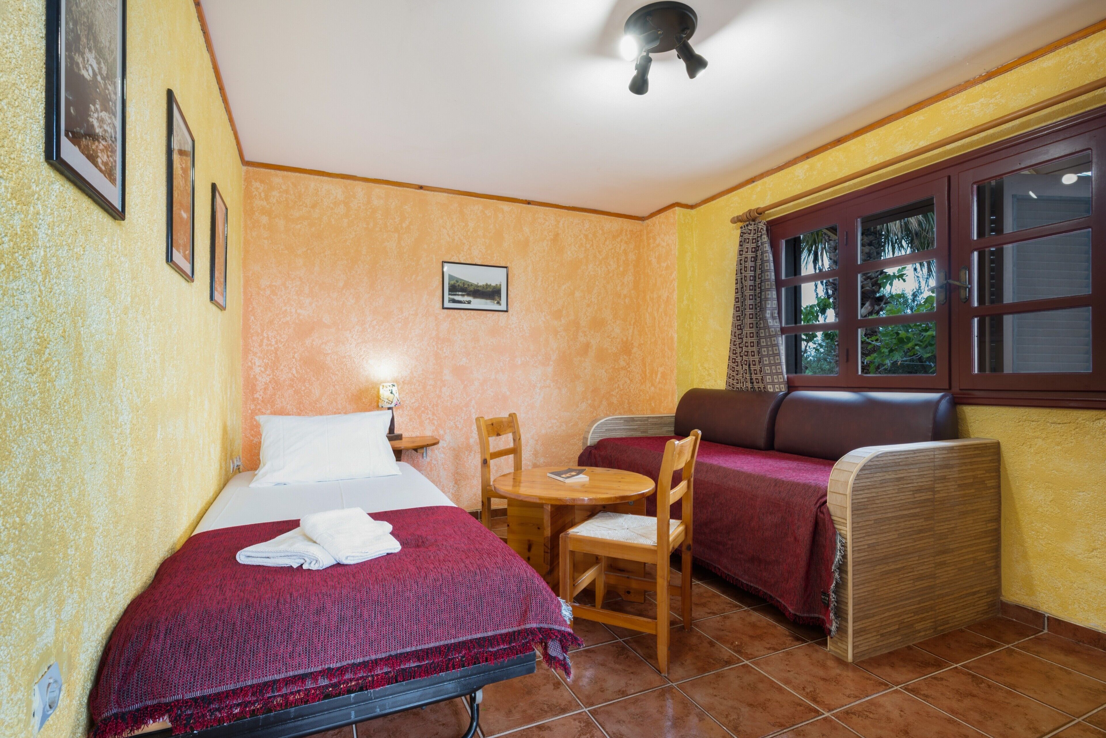 Una habitación con cama, una mesita, una silla, un sofá y una ventana con cortinas.
