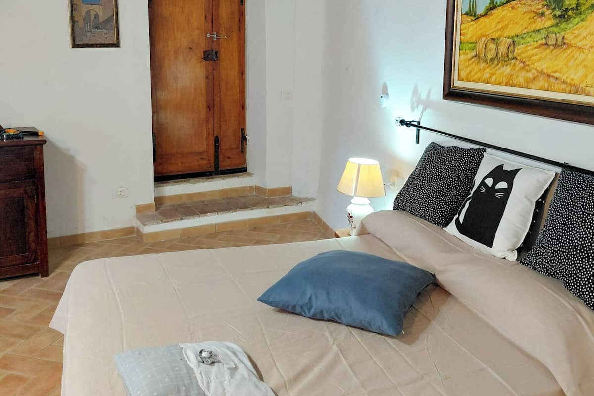 A bedroom with a bed, a wooden door, a painting, and a lamp.