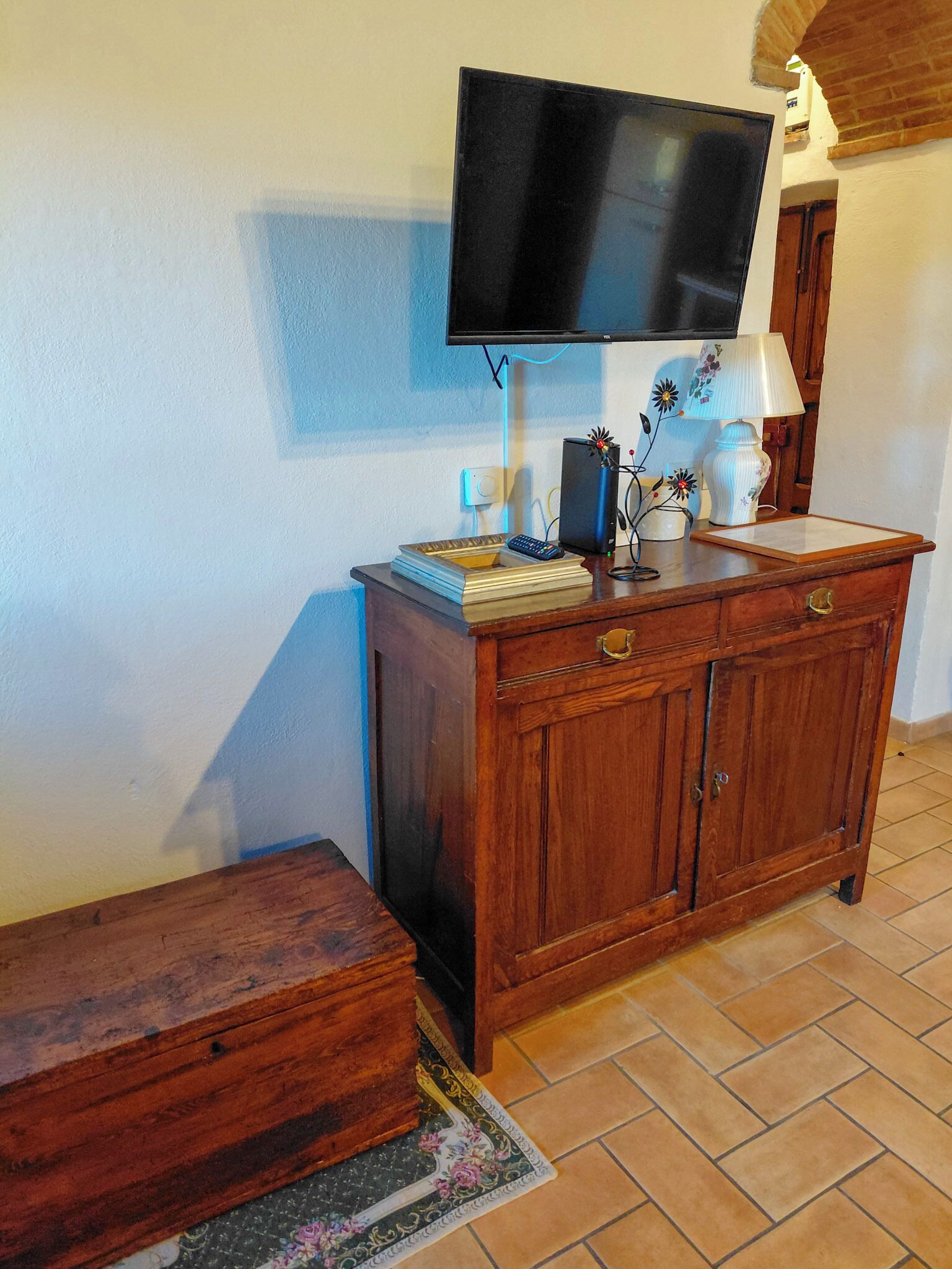 Ein Holzkabinet mit einem flachbildfernseher darüber, einer Lampe und einer kleinen Dekorationsvase auf der Ablagefläche.