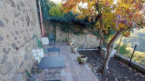A patio with a table and benches, surrounded by stone walls and a tree. - La Dimora di Dida (Seggiano)