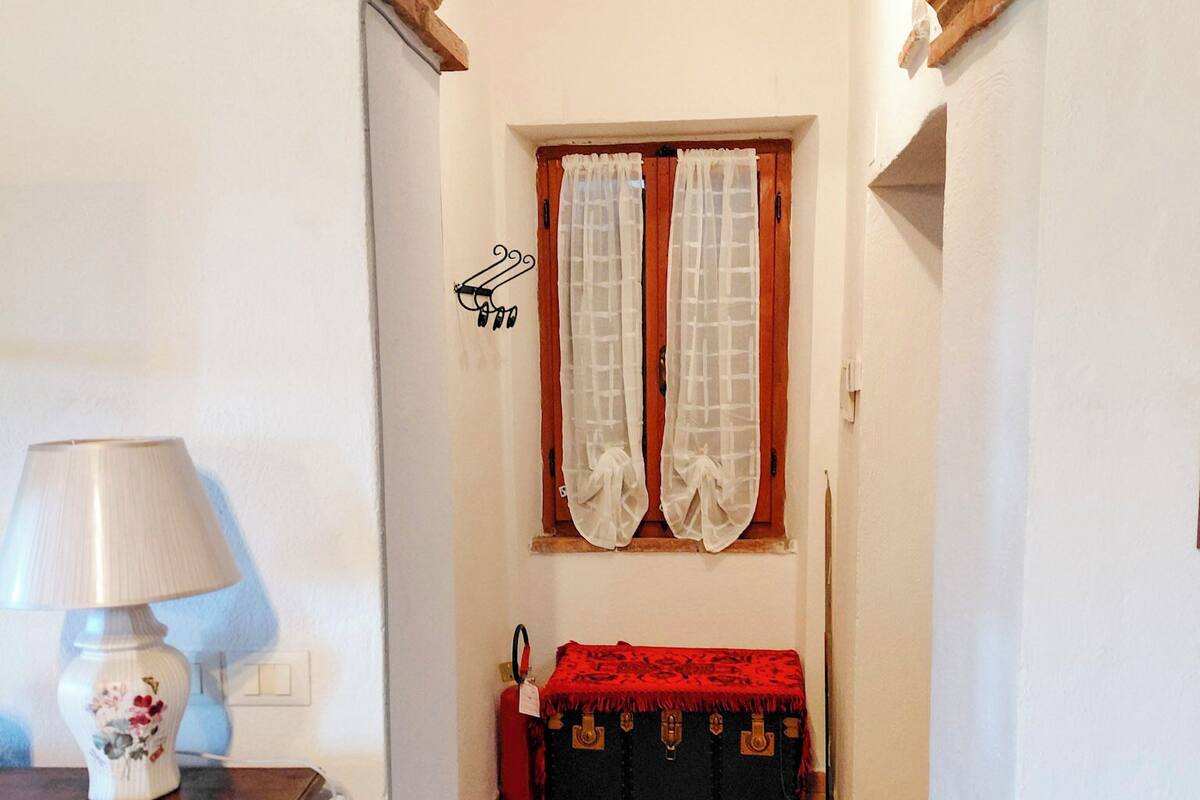 A narrow hallway with a brick archway, a window with sheer curtains, a red bench, and a lamp on a table.