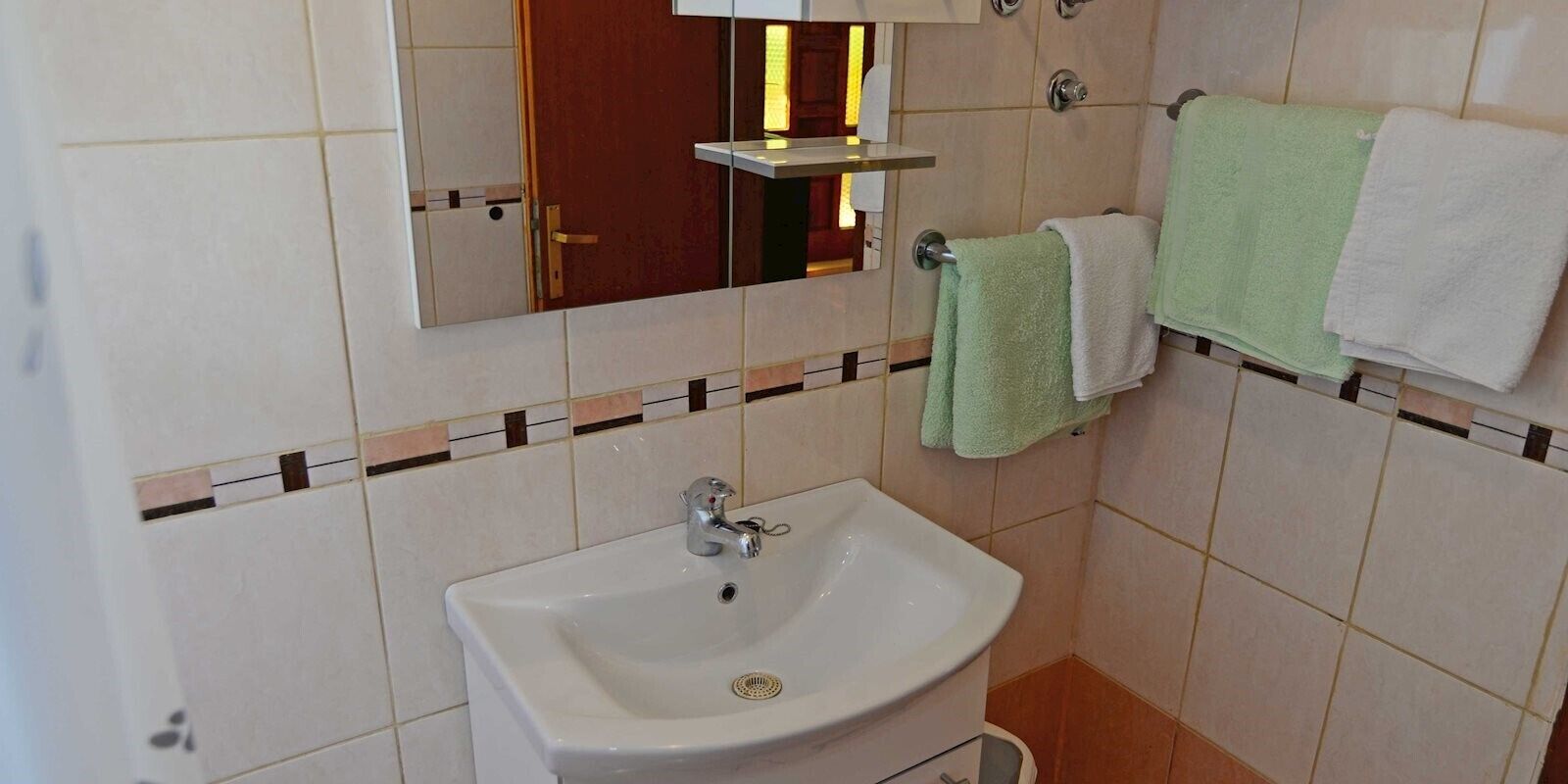 A bathroom with a white sink, a mirror, and two towels hanging on the wall.