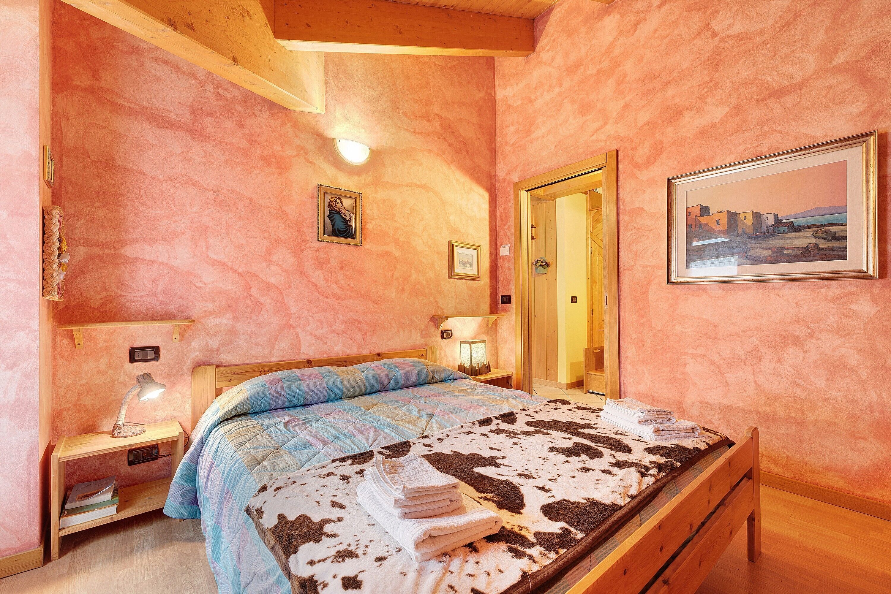 Un dormitorio con cama, mesita de noche, lámpara y un cuadro en la pared.