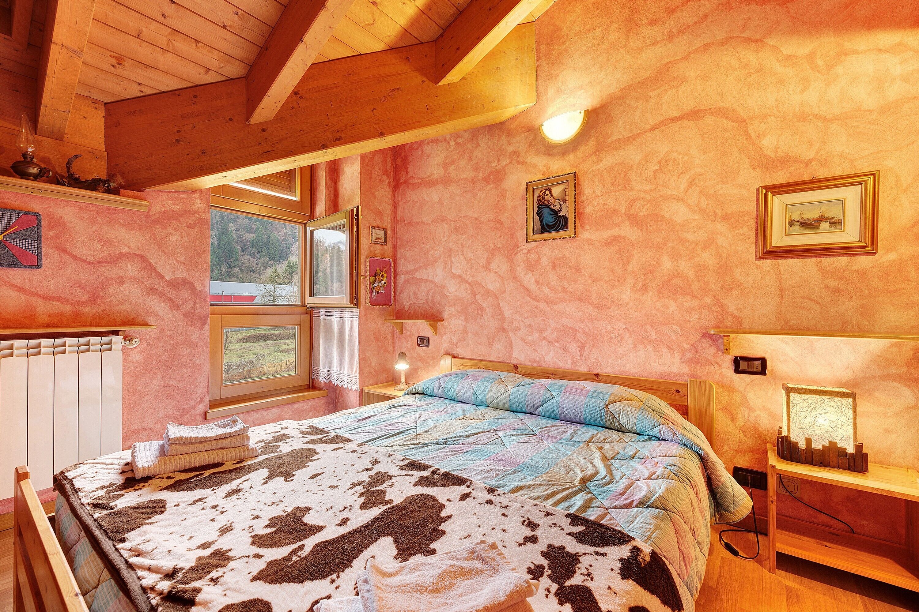 Una camera da letto con un letto, un comodino, una lampada, una finestra e una parete con quadri.