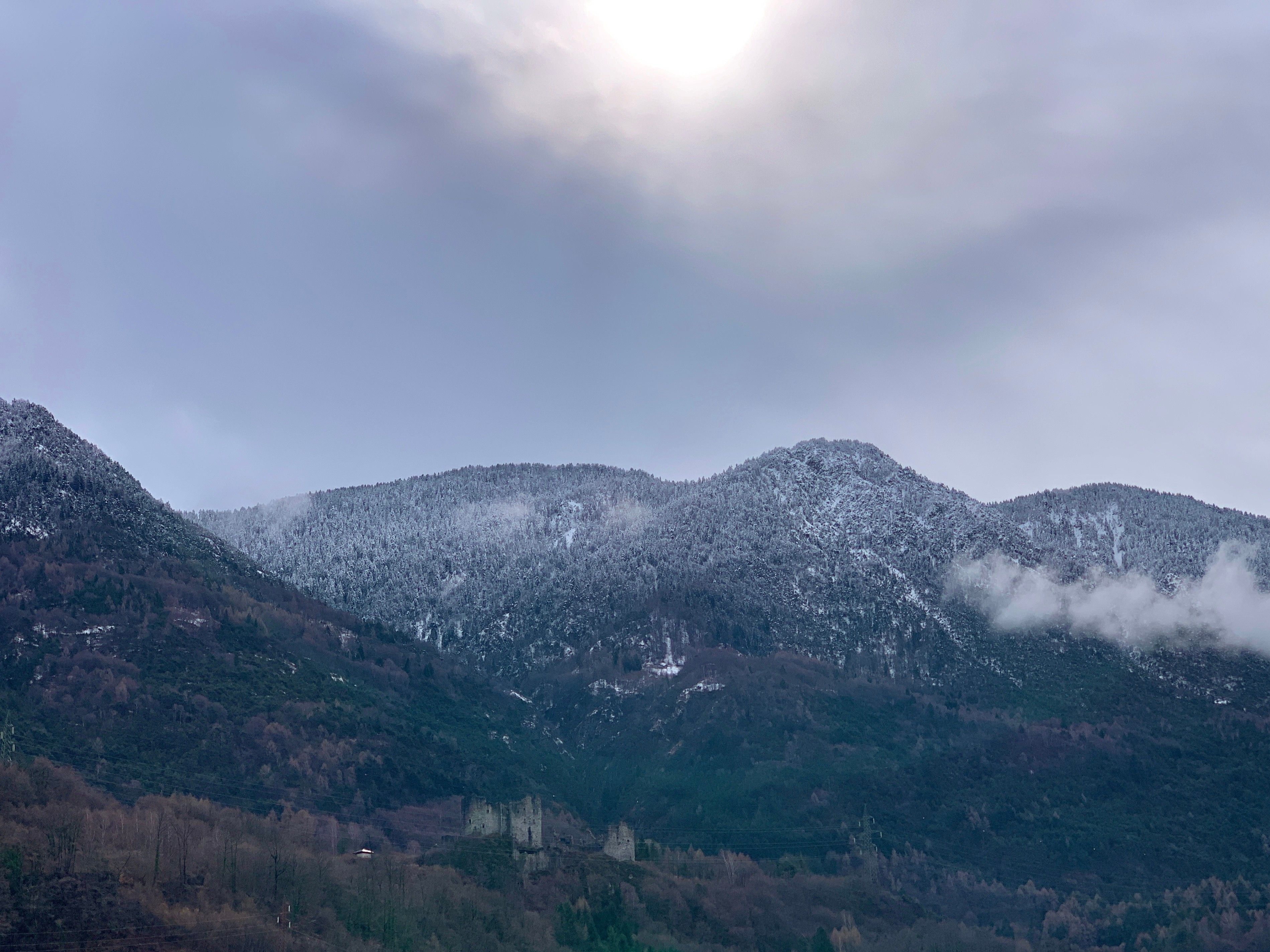 Een bergachtig landschap met besneeuwde toppen en een kasteelachtige constructie op een heuvel.