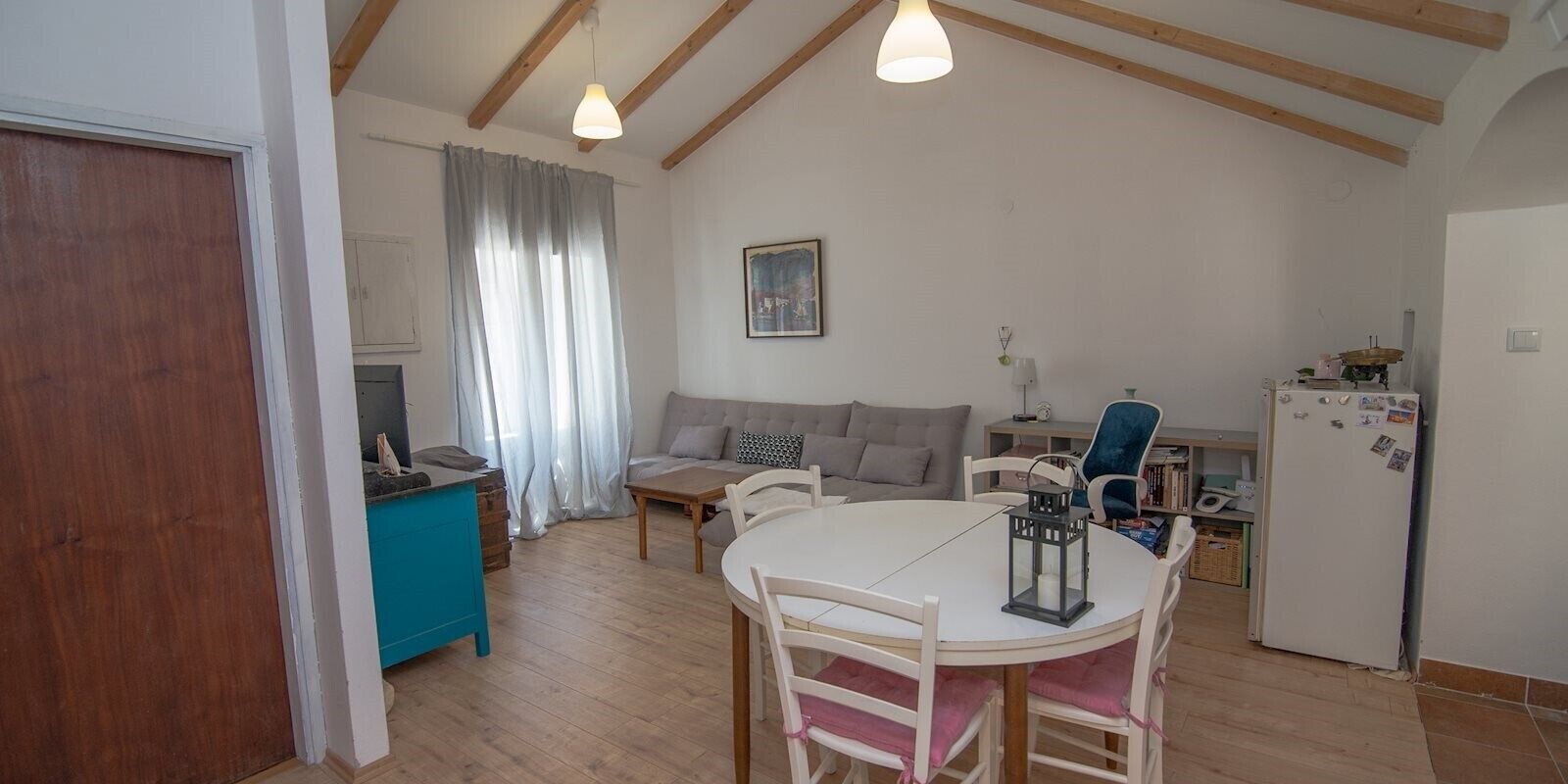 Een gezellige woonkamer met een witte bank, een blauwe kast en een eettafel met stoelen.