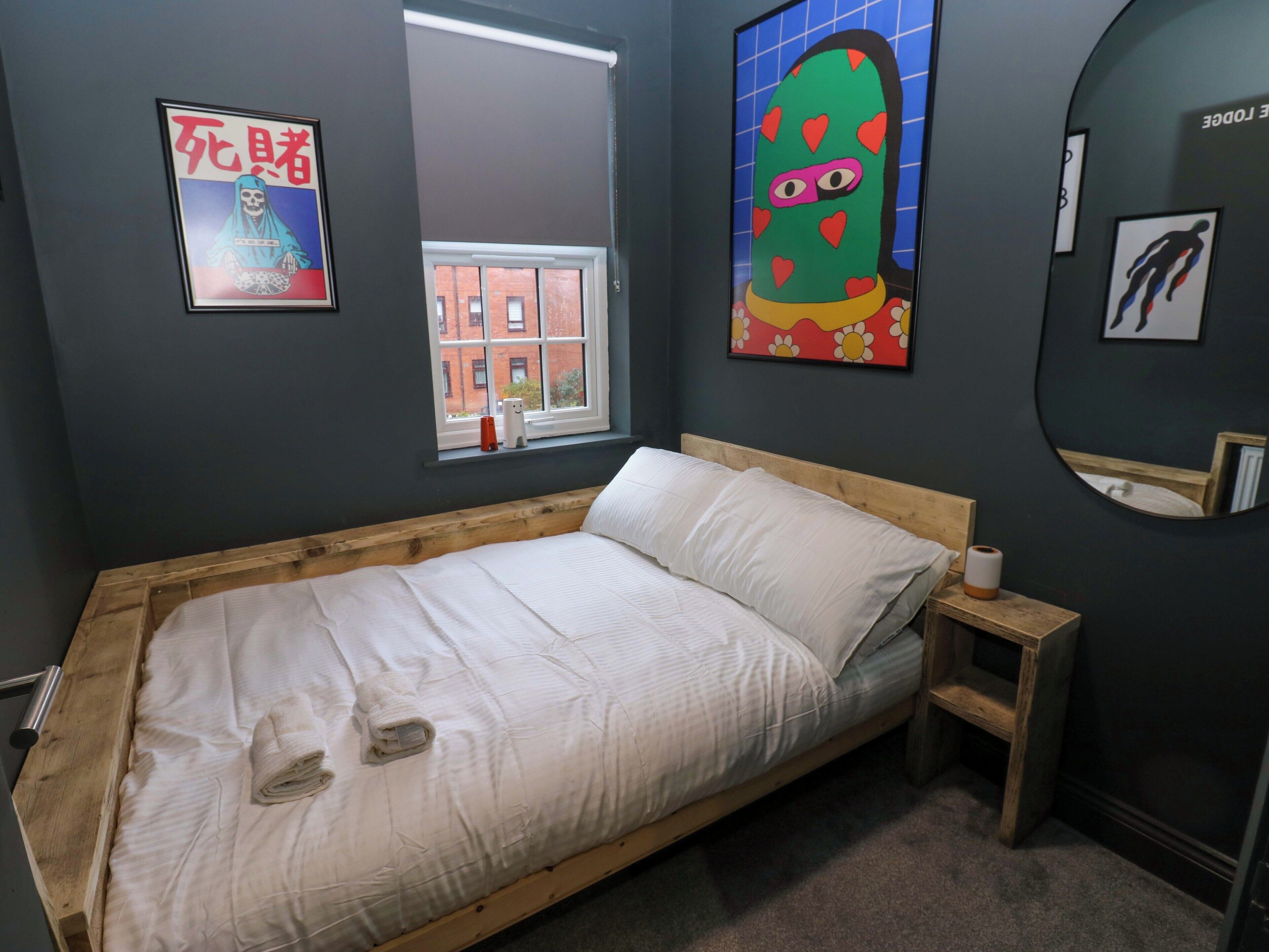 Un dormitorio con una cama de madera, una ventana, un espejo y dos obras de arte en la pared.